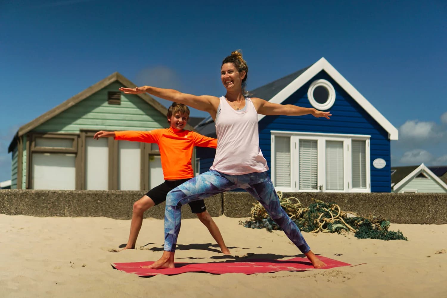 Beks teaching warrior pose on the beach with a young student joining in