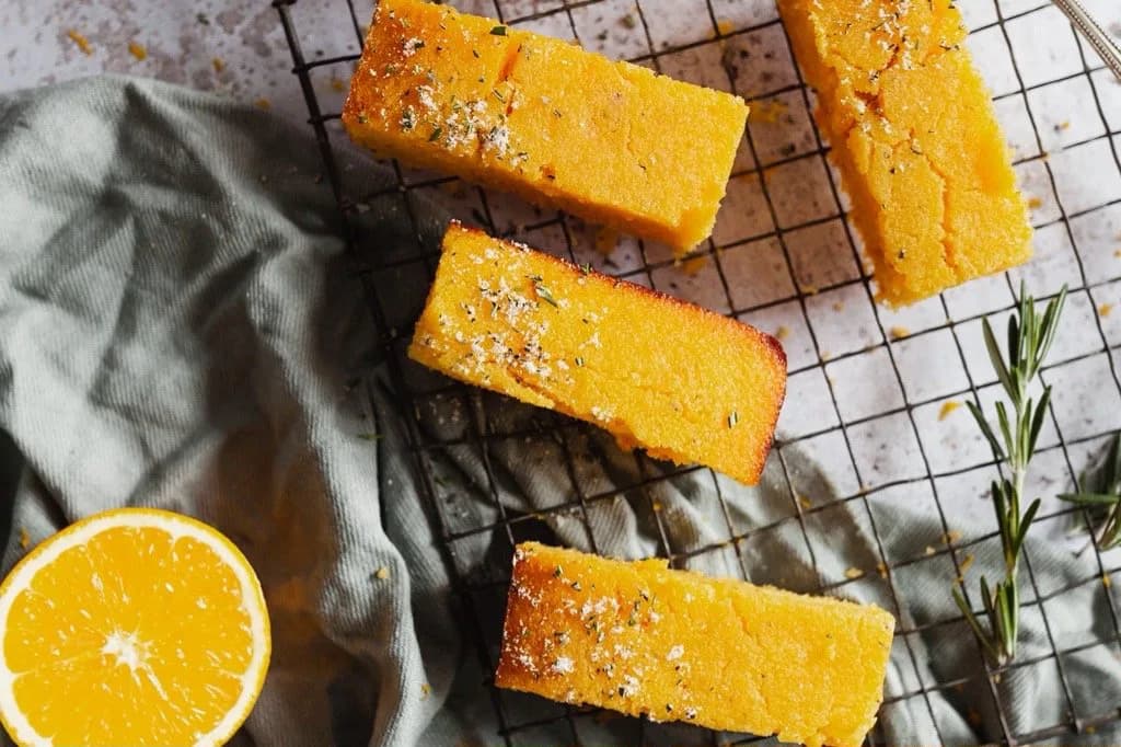 Slices of rosemary cornbread cooling on a wire rack beside fresh orange