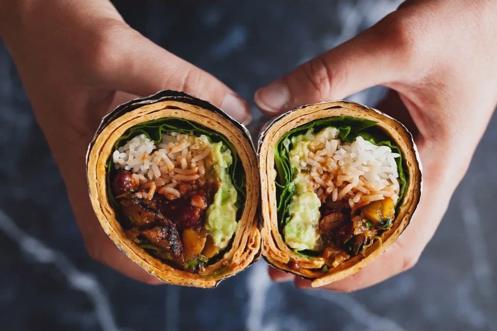 Hands holding freshly made vegan wraps filled with rice, avocado and greens